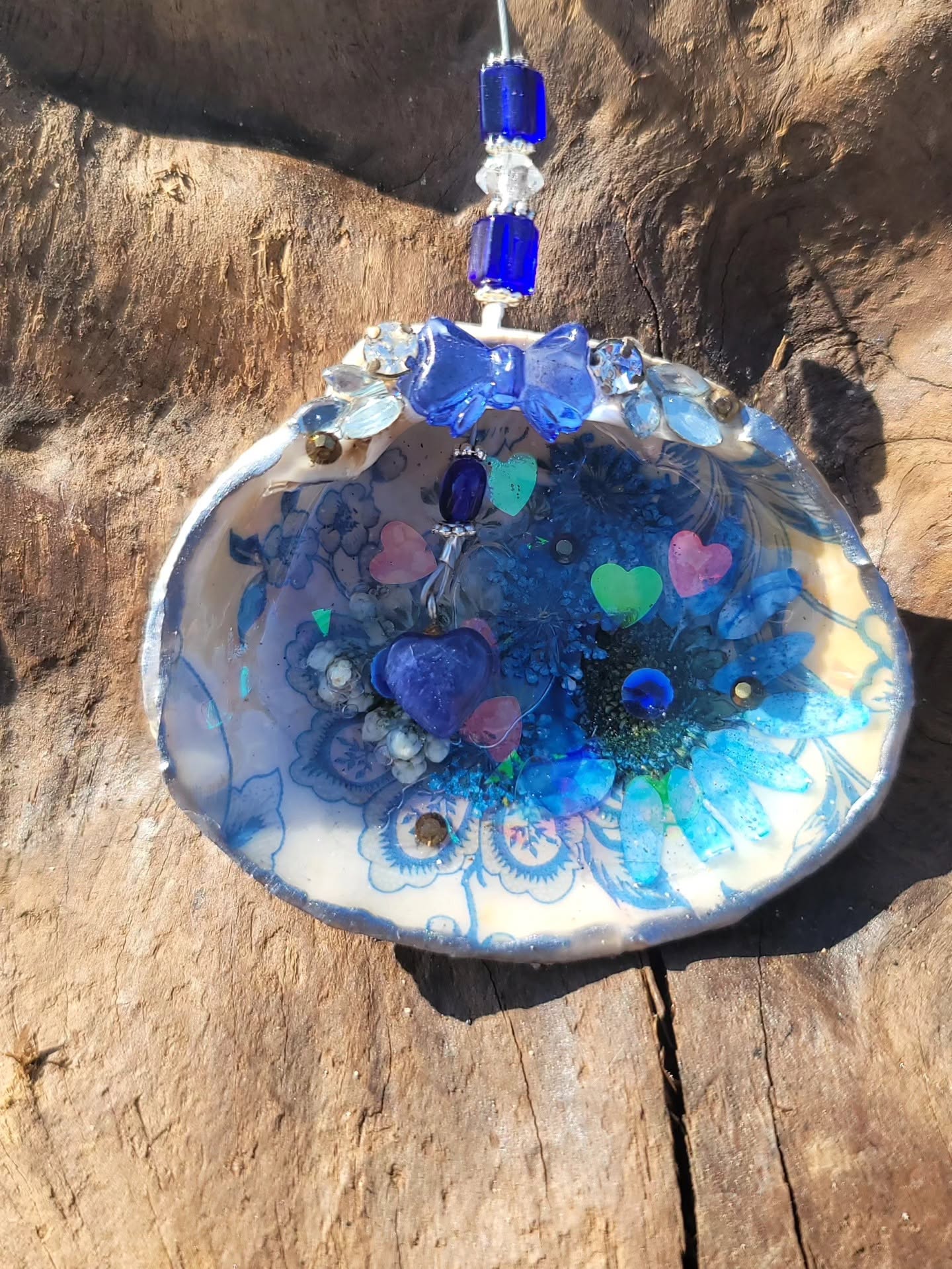 Hanging blue floral shell with hearts, bow, and cobalt beads on driftwood